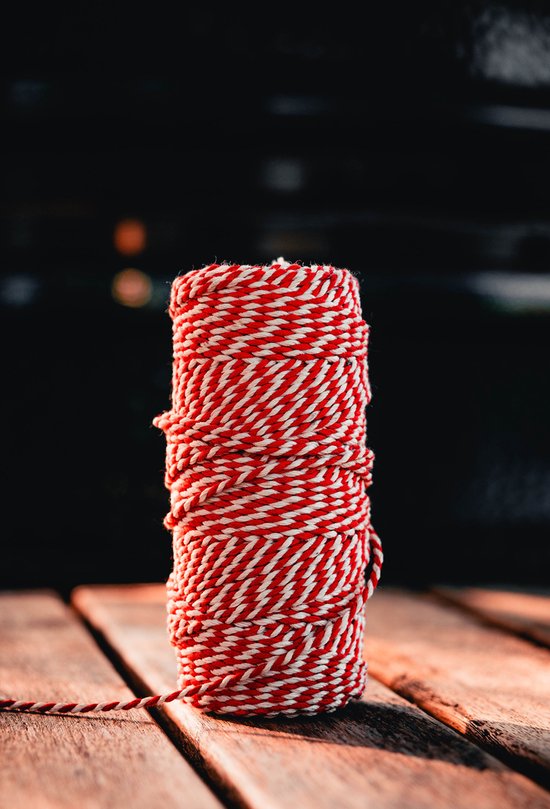 Een rol rood met wit gevlochten keukentouw op een houten ondergrond.