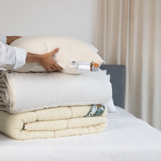 Handen pakken een stapel textiel: een kussen, een dekbed, een schapenvacht.