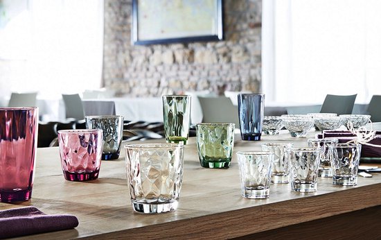 Verres colorés Bormioli Rocco de différentes tailles et couleurs, dont rose, vert et bleu, sur une table en bois.