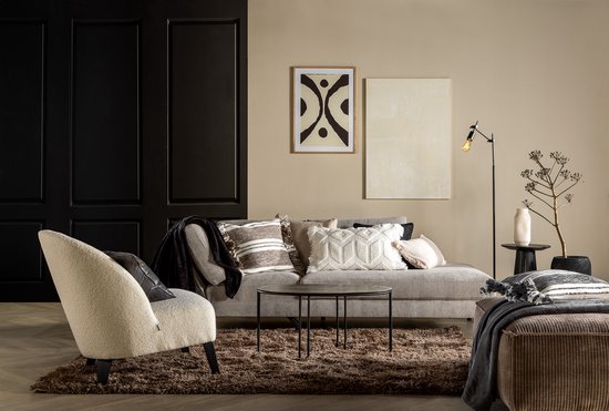 Een woonkamer met een grijze hoekbank, een fauteuil, bijzettafels en decoratieve kussens.
