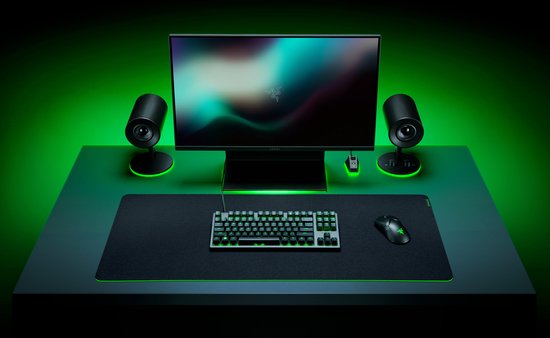 Bureau met een opstelling voor gaming, met een muismat, toetsenbord, muis, monitor en speakers, met groene accentverlichting.