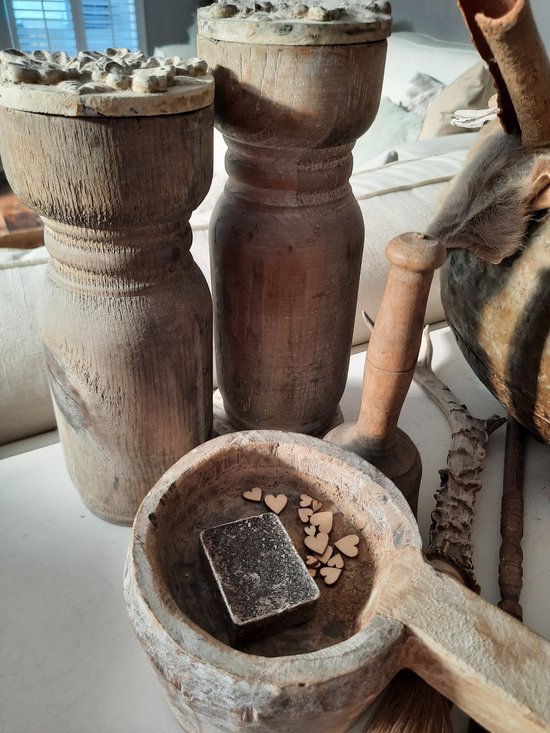 Een vierkant, donkergrijs amberblokje met ruw oppervlak, in een houten lepel met houten hartjes.