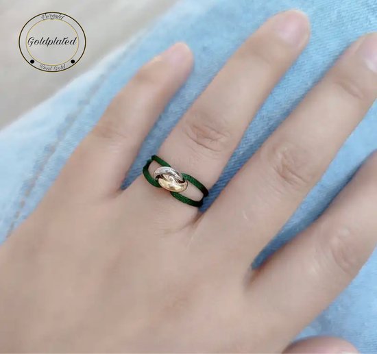 Gouden en zilveren ring met drie in elkaar gedraaide cirkels op een groene koord, gedragen op een vinger.