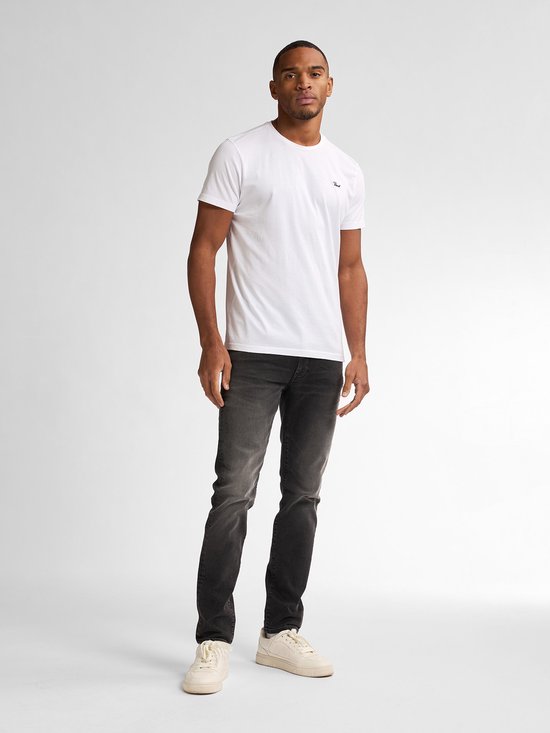Man draagt een witte t-shirt en zwarte slim fit jeans met vintage wassing.
