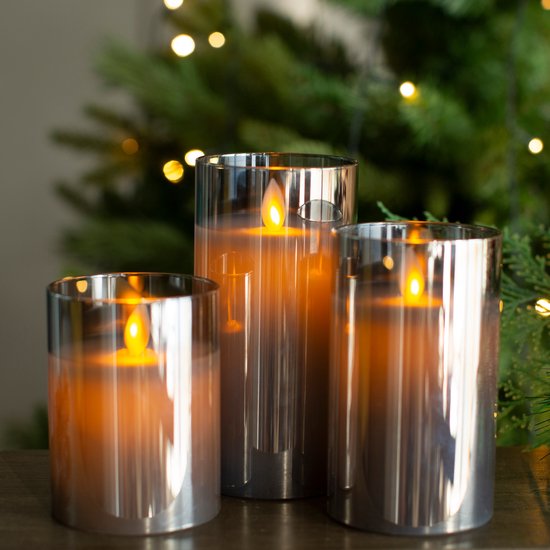 Drie LED kaarsen met bewegende vlam in glazen potten. De kaarsen hebben een amberkleurige gloed en staan voor een kerstboom.