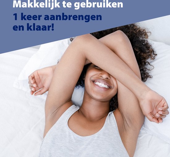Vrolijke vrouw met krullend haar ligt in bed, bedekt haar gezicht met haar armen.