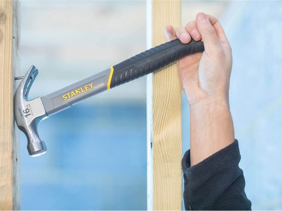 Hand die een grijze en zwarte klauwhamer met gele accenten gebruikt om een spijker in hout te slaan.
