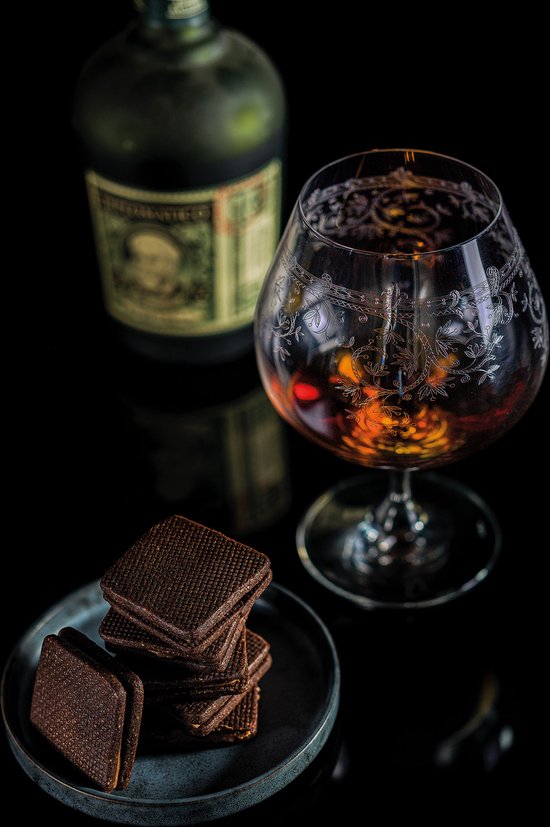 Verre à brandy avec une liqueur ambrée, des carrés de chocolat glacés et une bouteille en arrière-plan.