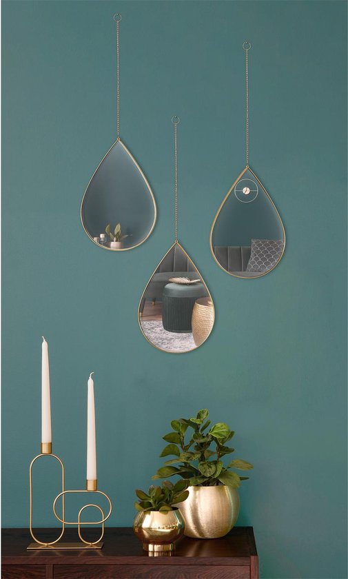 Drie druppelvormige spiegels met gouden frame hangend aan een muur met kaarsen en planten.
