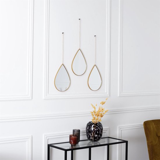 Drie druppelvormige spiegels met gouden frame hangend aan een witte muur met een vaas.