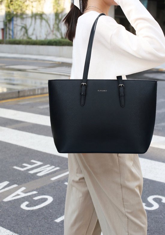 Zwarte Eleganci shopper gedragen door een vrouw met een witte trui en beige broek, op een zebrapad.