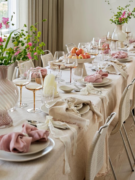 Gedekte tafel met crèmekleurig servies, roze servetten en glazen.