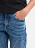 Detail van een blauwe jeans met een hand in de zak. De jeans heeft lichte wassingen en oranje stiksels.