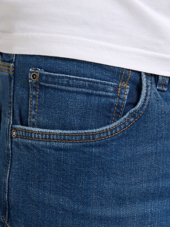 Detail van de voorkant van een blauwe spijkerbroek met een coin pocket, rits en knoopsluiting.