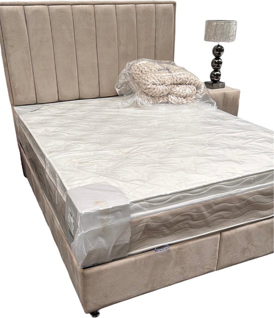 Beige boxspring met gestreept hoofdbord, matras en topper. Een plaid ligt op het matras.