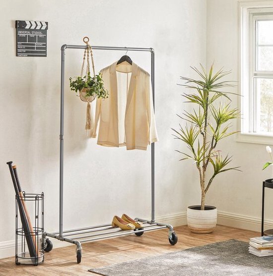 Verchroomd kledingrek op wieltjes met een jasje en schoenen. Hangplant en plantenbak ernaast.