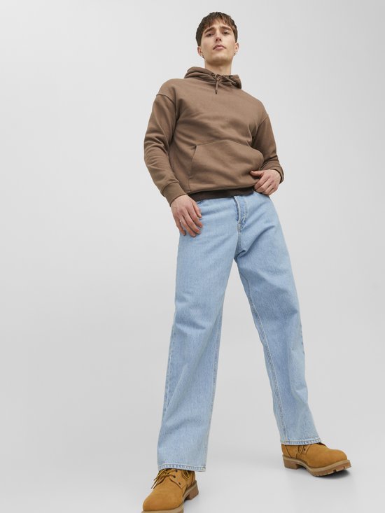Man van onderaf gefotografeerd, in een lichtblauwe jeans en een bruine hoodie.