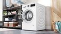 Witte Bosch Serie 6 wasmachine met open deur, naast een kledingkast met wasgoed.