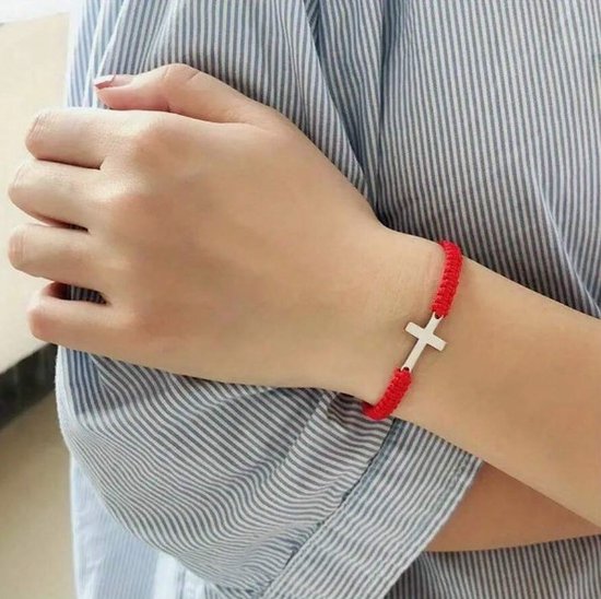 Een vrouwelijke pols met een rode kruisarmband.