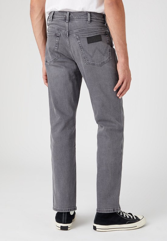 Man, van achteren gezien, in een grijze jeans. Hij draagt zwarte sneakers.
