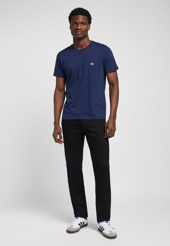 Man in een marineblauw T-shirt en zwarte jeans, met witte sneakers met strepen.