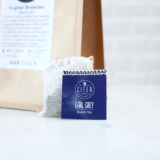 Close-up van een blauw CITEA 'Earl Grey Black Tea' kaartje en een wit theezakje voor een bruine papieren zak.