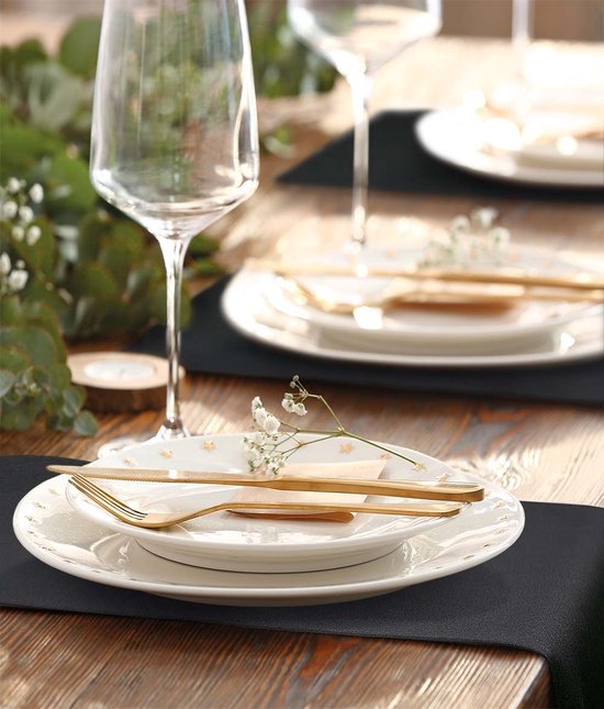 Zwarte placemats op een houten tafel, gedekt met witte borden en gouden bestek.