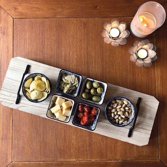 Houten plank met zes tapas schaaltjes gevuld met snacks en twee kaarsen.