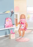 Een baby Born pop met masker in een roze outfit, houdt een thermometer vast.
