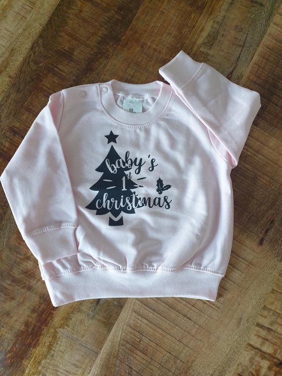 Roze babysweater met zwarte opdruk 'baby's 1st christmas' en een kerstboomfiguur.
