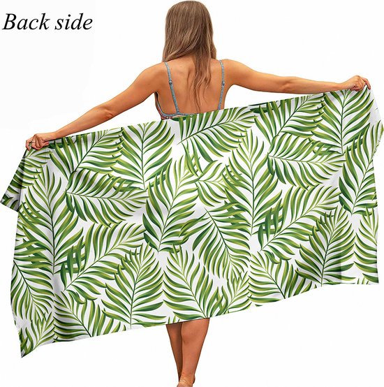 Vrouw met de rug naar de kijker toe, toont een badhanddoek met witte achtergrond en groene tropische bladeren.