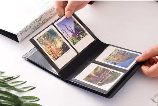 Open zwart fotoalbum met vier foto's, waaronder lavendel en een boom. Handen plaatsen een foto erin.