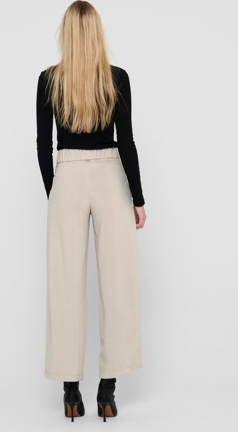 Model op de rug gezien, draagt een zwarte top en beige wijde broek met elastische tailleband.