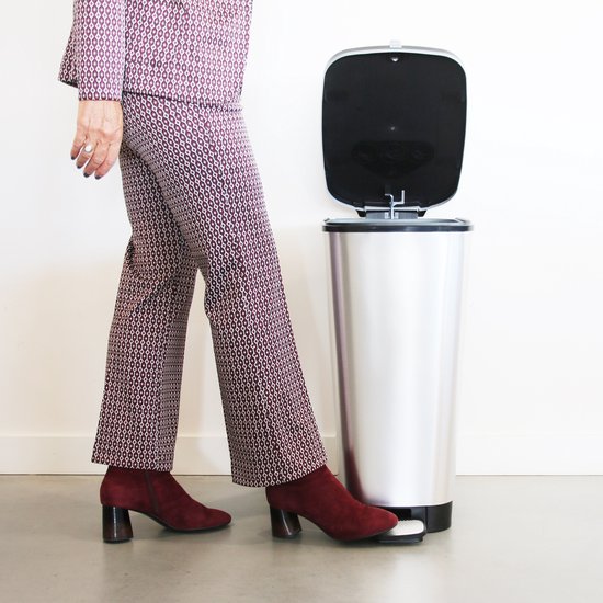 Personne portant un tailleur violet et blanc à motifs géométriques et des bottines rouges ouvre une poubelle argentée avec la pédale.