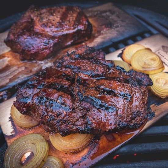 Twee sappige, gegrilde steaks op cederhouten planken, met ringen van gegrilde ui.
