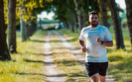 Homme portant un t-shirt de sport blanc Rogelli et un short noir, pouces levés, courant sur un chemin forestier.