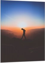 WallClassics - Vlag - Silhouet Persoon tussen de Bergen bij Zonsondergang - 70x105 cm Foto op Polyester Vlag
