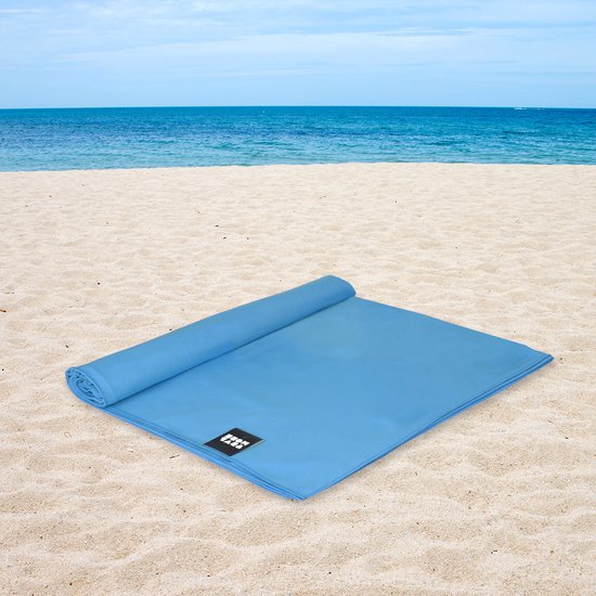 Opgerolde blauwe microvezelhanddoek op een zandstrand met de oceaan op de achtergrond.