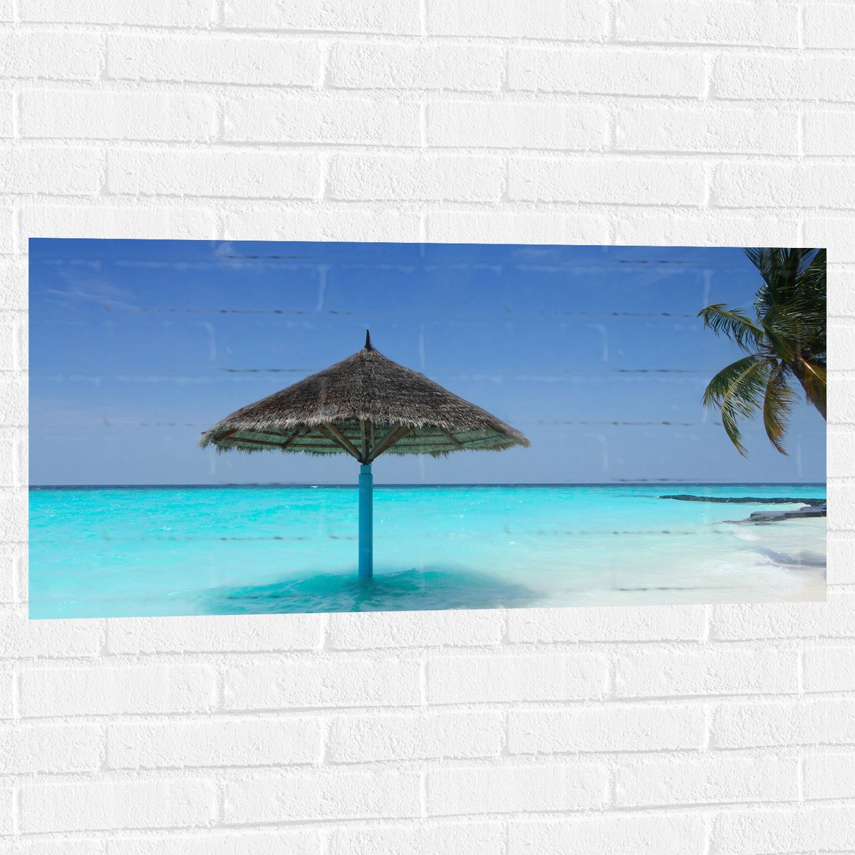 Muursticker - Rieten Parasol op het Strand bij het Blauwe Water - 100x50 cm Foto op Muurst