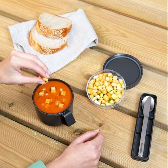Un ensemble de couverts Brabantia dans un étui gris foncé à côté d'un bol de soupe et d'un récipient de croûtons.
