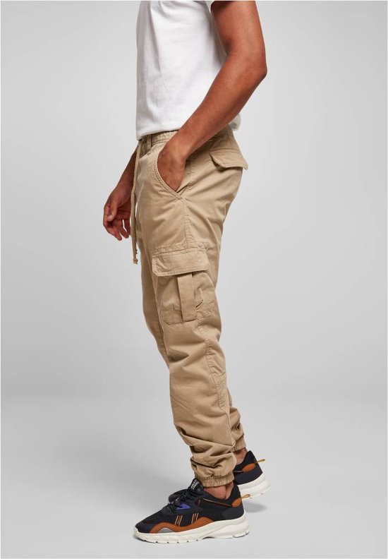 Man in beige cargo broek met trekkoord, zijdezichtbaar, met zakken en elastische enkelbanden.