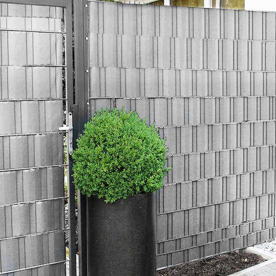 Grijze vlechtband voor een hek, met een groen struikje in een pot ervoor.