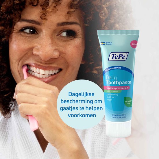 Vrouw met krullend haar poetst haar tanden met een roze tandenborstel. Een tube TePe Daily Toothpaste staat ernaast.