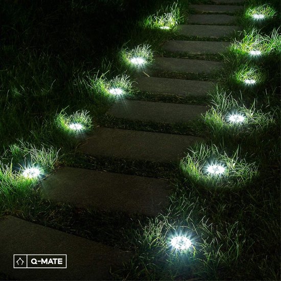 Allée de jardin éclairée avec des dalles de pierre, entourée d'herbe avec 10 spots à lumière blanc chaud.