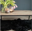 Salontafel met licht houten blad en zwart stalen frame. Een boeket roze tulpen en glazen windlichten met kaarsen. Zwart schapenvachtje eronder.