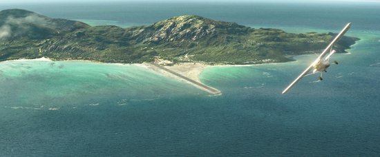 Vliegtuigje vliegt over een tropisch eiland met landingsbaan in zee.