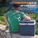 Een man met een groene T-shirt en een witte pinguïn erop zit op een muurtje naast een blauwgrijze koelbox.