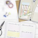 Bovenaanzicht van een opengeslagen bullet journal met dagen van de week en highlights, naast een etui met pastelkleurige markeerstiften.