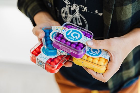 Handen houden drie IQ Mini spelletjes vast in rood, paars en geel.