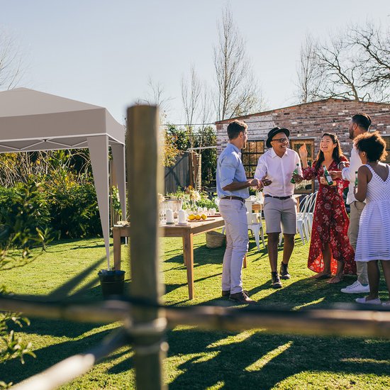 Beige partytent opgesteld in een tuin, met mensen die aan tafel zitten.